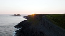 Dramatic Rocky Coast Line And Beautiful Grassy Hills With Setting Sun Over Open Sea