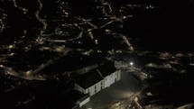 Drone orbits to the right as it descends in front of Igreja de Nossa Senhora das Merces e Perdoes at night