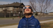 Young boy quickly looks at eclipse then turns away with glasses on
