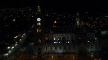 Aerial shot drone flies slowly to right on side of the Basilica del Voto in Quito at night