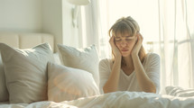 AI Generated Image. Frustrated woman with autism sitting on a bed at the morning and covering ears with pillow