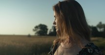 Sunlight shines on woman in grass field during summer sunset.