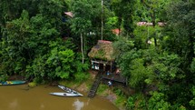 Aerial shot drone flies toward and then straight up in front of lodge on brown river in middle of Amazon rainforest