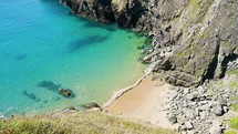 Slow panning shot of stunning cove along dramatic rocky coast line with blue waters