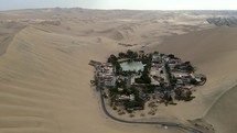 Aerial shot drone pans left in wide shot of desert city oasis Huacachina, Peru