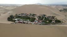 Aerial shot drone flies over sand dune to reveal desert city oasis Huacachina, Peru