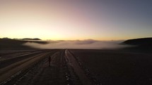 Aerial shot drone ascends over road leading into fog covered valley just before sunrise