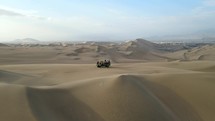 Aerial shot drone flies up and away from dune buggy in middle of sand dunes outside desert city oasis Huacachina, Peru