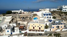 Aerial shot drone medium shot orbits right at Thera, Santorini with iconic three bell church with blue dome