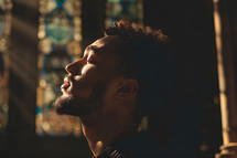 young Man worshiping in prayer, eyes closed, sunshine coming through window onto his skin, father 