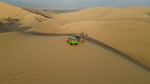 Aerial shot drone flies forward and orbits to the right around sandboarders going down dune near desert oasis Huacachina, Peru