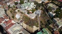 Aerial drone shot flies up close to funicular at popular tourist attraction on hill facing docks in coastal city on sunny day