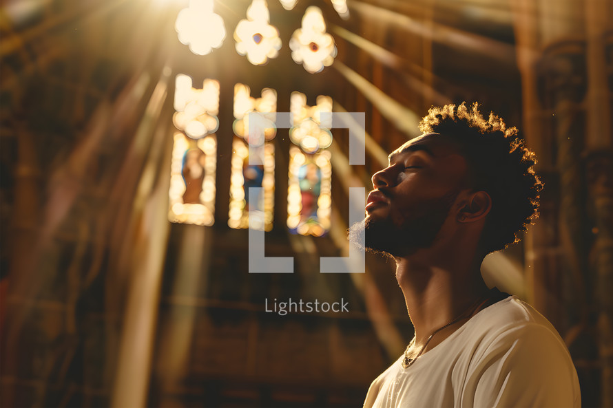 young Man worshiping in prayer in an English church, eyes closed, sunshine coming through window onto his skin, space for text