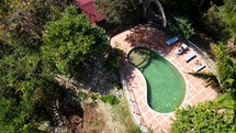 Aerial shot drone lowers as camera pans down over top of a pool at a resort on a mountain in the forest.