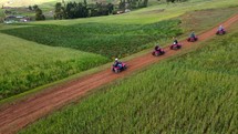 Aerial shot drone orbits to the right of five quad bikes traveling through green fields