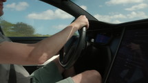 Man driving electric car down highway on sunny day - close up on hands and steering wheel