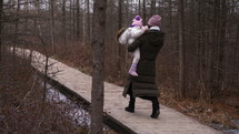 Mother takes toddler girl in arms to walk on nature path in late autumn - wide side