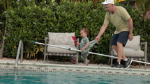 Father holding onto toddler daughter who is playing at edge of swimming pool
