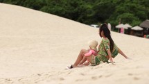 Mother and young daughter sand boarding in dunes on hot summer day - fun unique activity
