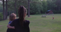 Mother holds baby daughter and walks towards young son at camp grounds during summer vacation - from behind