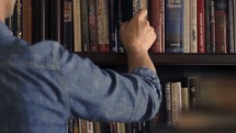 a man picking a book from a bookshelf 