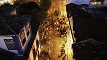 Drone hovers and then slowly flies forward over Holy Week procession in small South American town at night