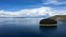 Aerial shot drone flies slowly backwards on Lake Titicaca with small forested island in middle of shot
