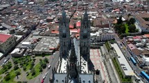 Aerial shot drone flies over the top of Basilica del Voto Nacional and pans up to see the two clock towers and the city of Quito