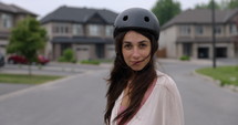 Female South American Latina skateboarder wearing helment on street looks towards camera