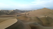Aerial shot drone flies backwards over sand dunes near desert oasis Huacachina, Peru with Ica in distance