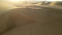 Aerial shot drone slowly flies backwards facing sun as sandboarder rides down dune on stomach near desert oasis Huacachina, Peru