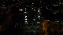 Aerial shot drone flies backwards from the front of the Basilica del Voto Nacional in Quito at night