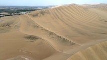 Aerial shot drone flies forward over sand dunes to west of desert city oasis Huacachina, Peru
