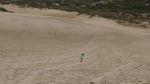 Boy sandboarding down dune hill in front of beach on summer day - wide - visualization success