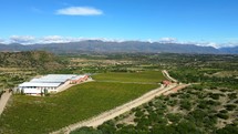 Aerial shot drone orbits to the right around front of bodega and vineyard at base of hill