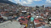 Aerial shot drone descends in front of central market with Basilica del Voto Nacional and city of Quito in background