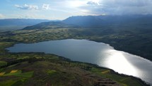 Aerial shot drone slowly glides forward over top of large hill overlooking Lake Huaypo with sun reflecting off surface