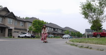 Female South American Latina skateboarder cruising around neighbourhood on board - wide follow shot