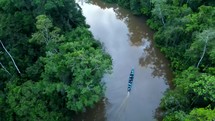 Aerial shot drone slowly ascending over water as motorized canoe boat goes down brown river in middle of Amazon rainforest