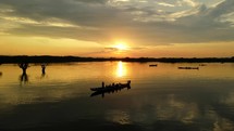 Aerial shot drone slowly rises with silhouettes of canoe boats floating on black lagoon in middle of Amazon rainforest at sunset