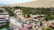 Aerial shot drone flies up and away from hotel on lake at oasis in middle of desert in Huacachina, Peru