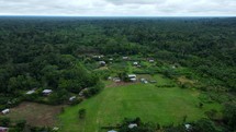 Aerial shot drone flying up and over lush green jungle in middle of Amazon rainforest to reveal indigenous village