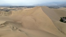 Aerial shot drone flies over dunes and slowly pans right facing desert city oasis Huacachina, Peru