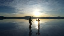 Aerial shot drone facing sunrise as silhouette couple jumps for joy on salt flats