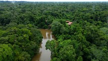 Aerial shot drone flies up and away from lodge on brown river in middle of Amazon rainforest