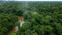 Aerial shot drone flies to right around lodge on brown river in middle of Amazon rainforest