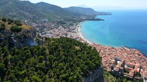 Aerial shot drone flies to the left as city of Cefalu, Sicily, Italy appears behind La Rocca