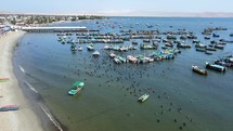 Aerial shot drone flies to right from beach in harbor full of boats and pelicans over wooden pier