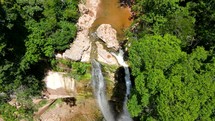 Aerial shot drone flies forward with camera facing down over top of waterfall as it goes up river and camera pans up to horizon