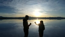 Aerial shot drone facing sunrise as silhouette couple does secret handshake on salt flats
